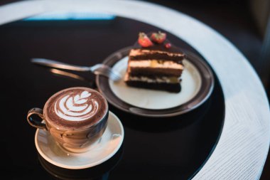CAPUCINO veya sütlü kahve ile bir pasta siyah bir tablo üzerinde beyaz bir fincan.