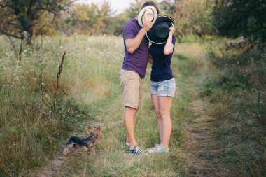 Genç çift küçük köpek ile yorkshire terrier giymiş t-shirt ve şapka kucaklayan ve yolda iyi eğlenceler