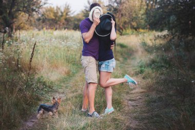 Genç çift küçük köpek ile yorkshire terrier giymiş t-shirt ve şapka kucaklayan ve yolda iyi eğlenceler