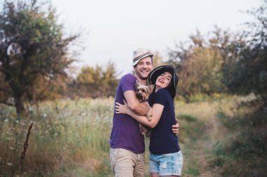 Genç çift küçük köpek ile yorkshire terrier giymiş t-shirt ve şapka kucaklayan ve yolda iyi eğlenceler