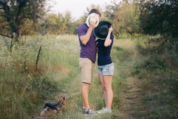Mladý pár s malým psem Jorkšírský teriér oblečené tričko a čepice objímat a bavte se na cestách — Stock fotografie