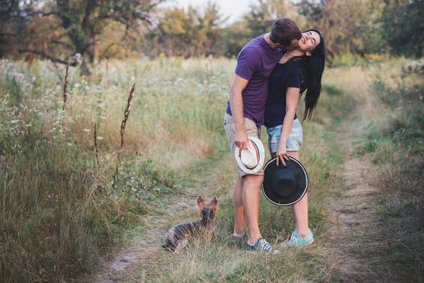 Young couple with little dog yorkshire terrier dressed  t-shirt and hat embracing and have fun on the road — Stock Photo, Image