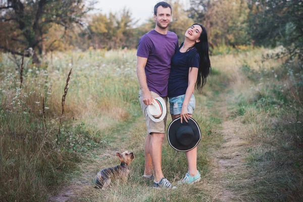 Genç çift küçük köpek ile yorkshire terrier giymiş t-shirt ve şapka kucaklayan ve yolda iyi eğlenceler