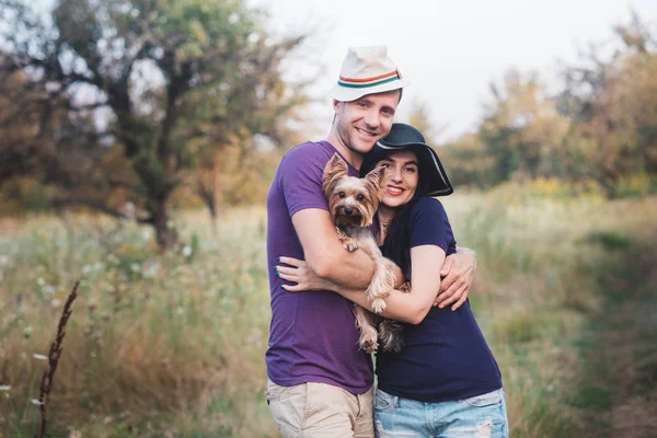 Casal jovem com pequeno cão yorkshire terrier vestido t-shirt e chapéu abraçando e se divertir na estrada — Fotografia de Stock