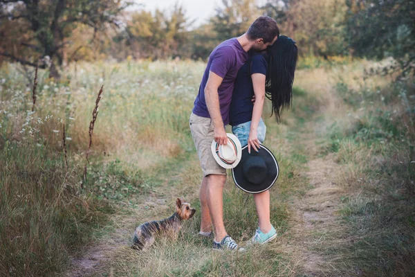 Unga par med liten hund yorkshire terrier klädd t-shirt och mössa omfamna och ha kul på vägen — Stockfoto