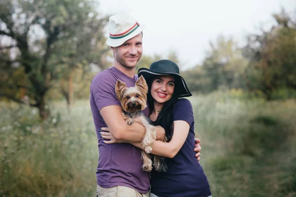 Genç çift küçük köpek ile yorkshire terrier giymiş t-shirt ve şapka kucaklayan ve yolda iyi eğlenceler