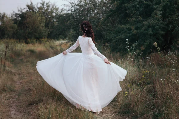 Yong bride spinning in a white dress on the bank on nature