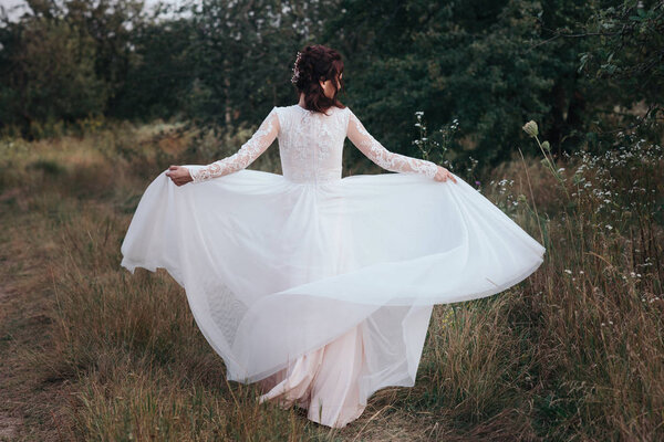 Yong bride spinning in a white dress on the bank on nature.Dress develops in the wind. Happy bride in a wedding dress is spinning.