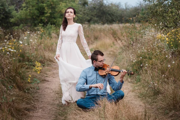 Violinista y mujer en vestido blanco, joven toca en el violín la naturaleza de fondo , — Foto de Stock