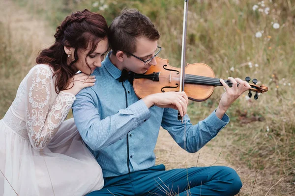 Hegedűművész és egy nő fehér ruhában, fiatal ember játszik a hegedű a háttérben természet, — Stock Fotó