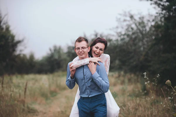 Жених несет невесту на руках на природе в лучах заката — стоковое фото