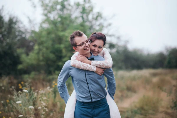 Just married loving hipster couple in wedding dress and suit on a green field in the woods.