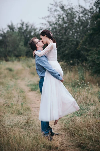 Жених несет невесту на руках на природе в лучах заката — стоковое фото