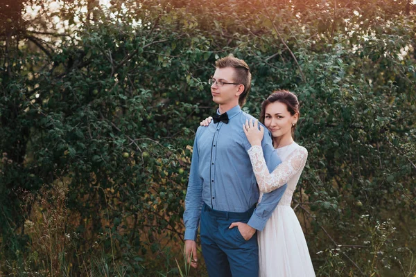 Только что вышла замуж за любящую пару хипстеров в свадебном платье и костюме на зеленом поле в лесу. — стоковое фото