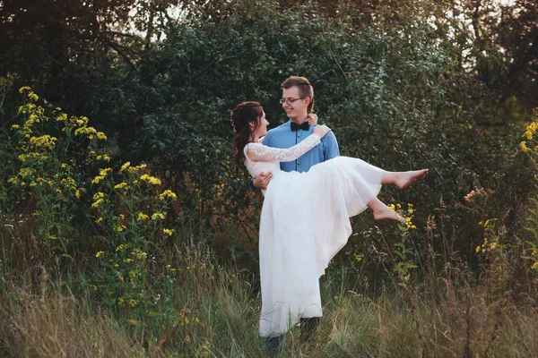 Γαμπρός νύφη μεταφέρει στην αγκαλιά του φύση με το φως του ηλιοβασιλέματος — Φωτογραφία Αρχείου