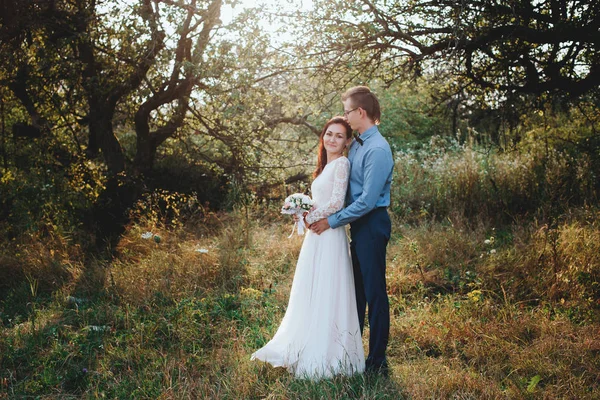Apenas casado casal hipster amoroso em vestido de noiva e terno em um campo verde na floresta. — Fotografia de Stock