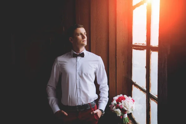 Close-up portrait of a young handsome guy groom delectable hipster in a suit and bow tie near the window