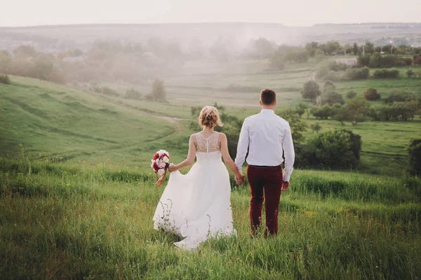 Jovem lindo casamento casal abraçando em um campo de volta para a câmera . — Fotografia de Stock