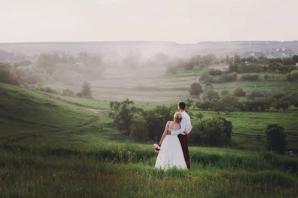 Casal encantador, noiva e noivo posando no campo durante o pôr do sol, estilo de vida — Fotografia de Stock