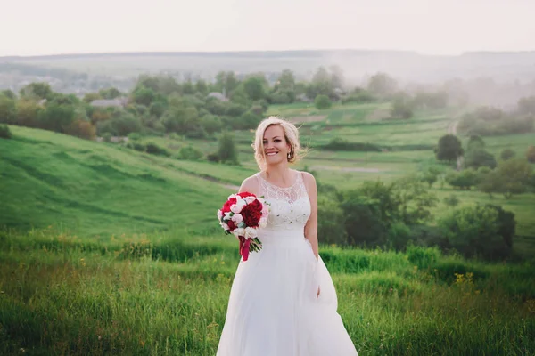 美丽的快乐和微笑新娘穿着婚纱，站在金色的夏天的田野 — 图库照片