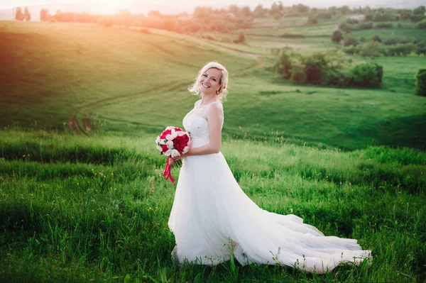 Belle mariée heureuse et souriante en robe de mariée debout dans les champs d'été dorés — Photo