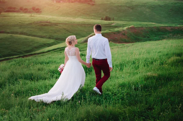 Jovem lindo casamento casal abraçando em um campo de volta para a câmera . — Fotografia de Stock