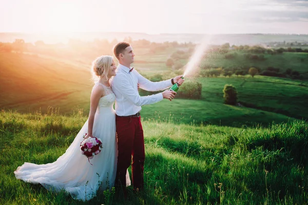 Casal de casamento feliz com buttle de champaine e salpicos de champanhe — Fotografia de Stock