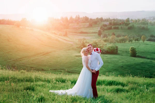 Casal encantador, noiva e noivo posando no campo durante o pôr do sol, estilo de vida — Fotografia de Stock