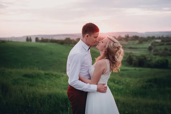 Прекрасная пара, невеста и жених позируют в поле во время заката, образ жизни — стоковое фото