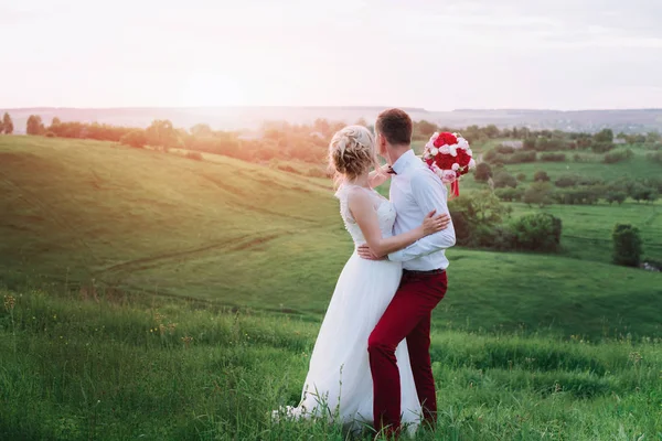 Jovem lindo casamento casal abraçando em um campo de volta para a câmera . — Fotografia de Stock