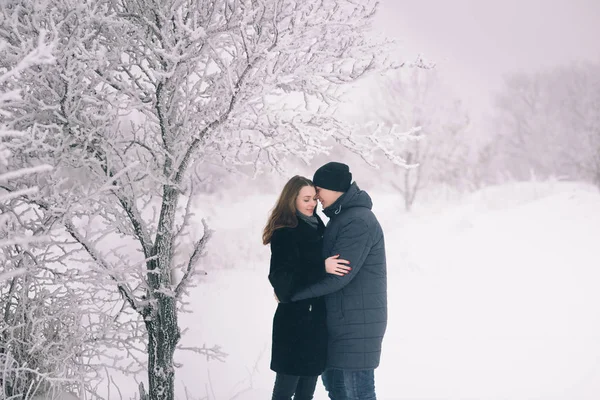 A loving couple on a winter walk. Snow love story, winter magic. Man and woman on the frosty street. The guy and the girl are resting on the snow. Christmas mood of a young family.