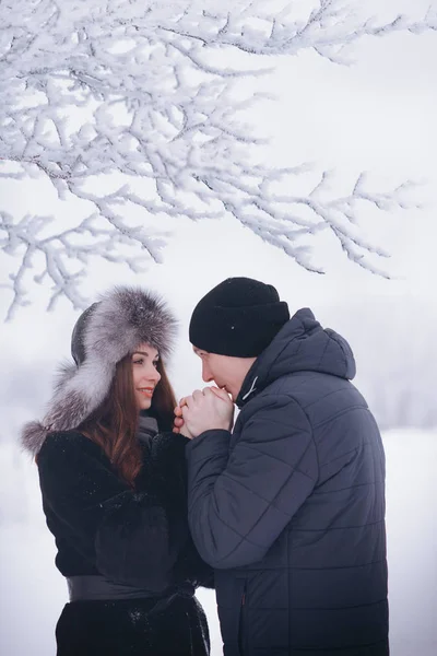 A loving couple on a winter walk. Snow love story, winter magic. Man and woman on the frosty street. The guy and the girl are resting on the snow. Christmas mood of a young family.