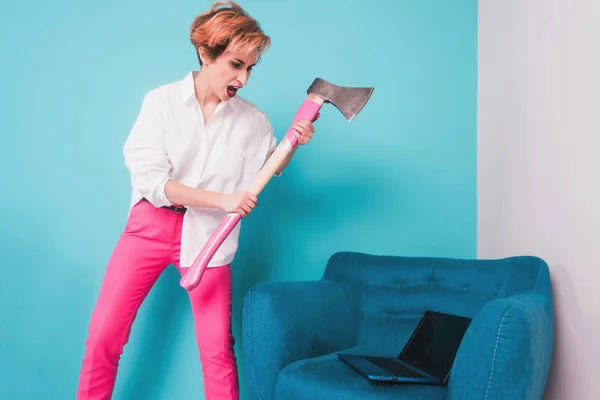 Angry furious businesswoman girl with an ax smashes a laptop, screaming. Negative human emotions, facial expressions, feelings, aggression, anger management issues concept