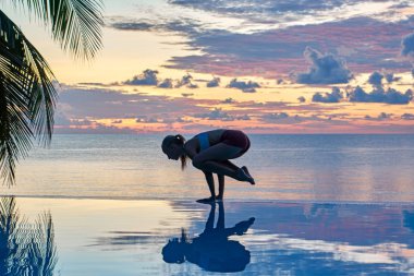 Genç bir kadın gün batımında deniz kıyısında yoga yapıyor. Seyahat konsepti. 