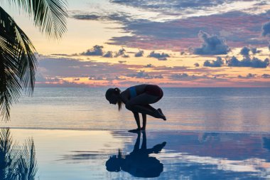Genç bir kadın gün batımında deniz kıyısında yoga yapıyor. Seyahat konsepti. 