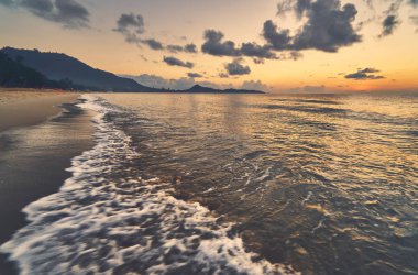 Güneşin doğuşunda kumlu kıyı şeridi ve deniz manzarası 