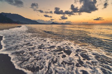 Güneşin doğuşunda kumlu kıyı şeridi ve deniz manzarası 
