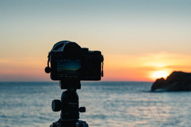 Gün batımında deniz kıyısında duran fotoğraf makinesinin görüntüsü 