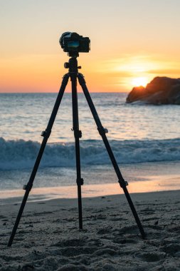 Gün batımında deniz kıyısında duran fotoğraf makinesinin görüntüsü 