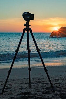 Gün batımında deniz kıyısında duran fotoğraf makinesinin görüntüsü 