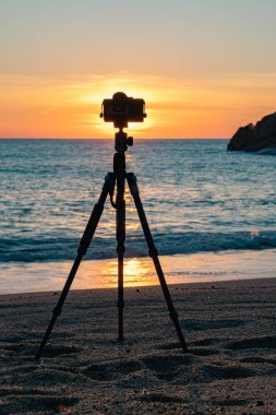 Gün batımında deniz kıyısında duran fotoğraf makinesinin görüntüsü 