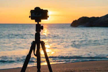Gün batımında deniz kıyısında duran fotoğraf makinesinin görüntüsü 