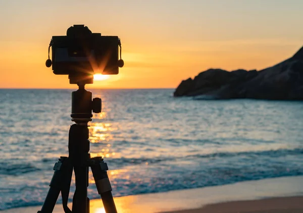 view of photo camera standing on sea shore on sunset background