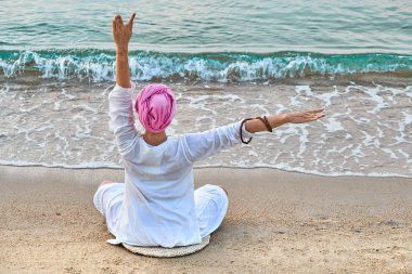 Renkli günbatımında deniz kıyısında yoga yapan genç bir kadın. Seyahat kavramı. 