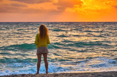 Sahilde renkli günbatımı arka planında duran kadının dikiz görüntüsü 