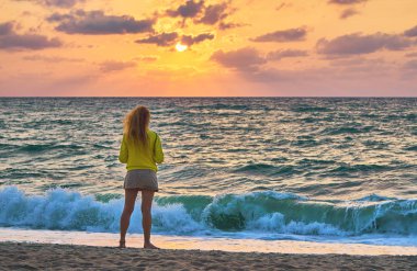 Sahilde renkli günbatımı arka planında duran kadının dikiz görüntüsü 