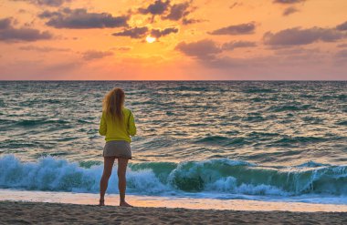 Sahilde renkli günbatımı arka planında duran kadının dikiz görüntüsü 