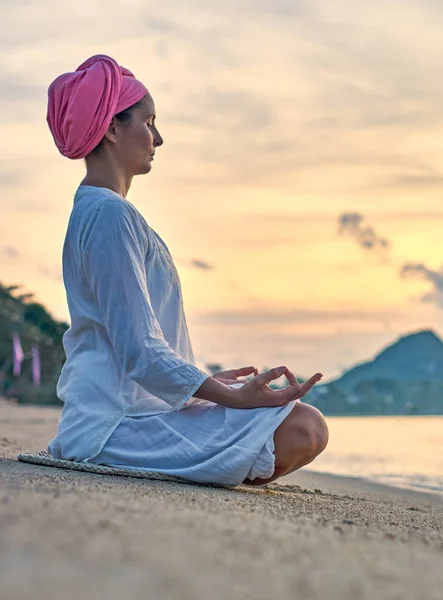 Young woman practicing yoga on sea coastline during colorful sunset, travel concept