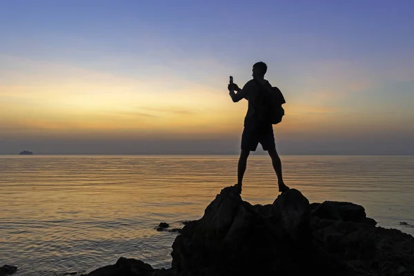 silhouette of male photographer at shore making shot of colorful sunset