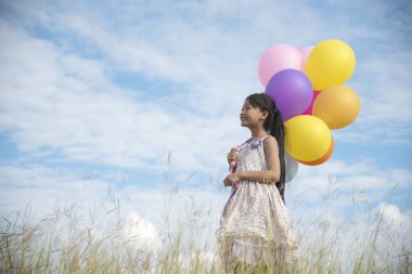 Mutlu kız renkli balon ile bulutlu ve mavi gök yeşil çayır üzerinde tutan
